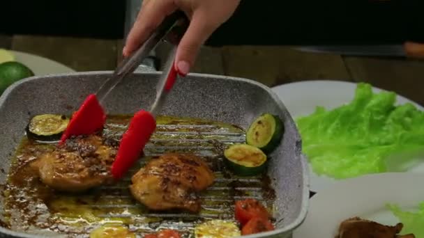Női kéz teszi csirke darabokat egy tányérra, zöld saláta — Stock videók