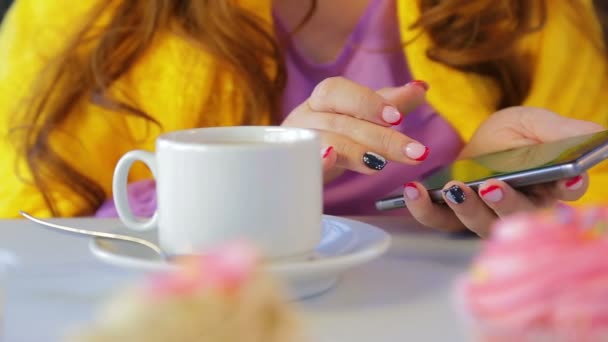 La chica en un café en la mesa con pasteles hojeando las noticias en el teléfono inteligente — Vídeos de Stock