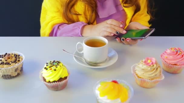 La chica en un café en la mesa con pasteles hojeando las noticias en el teléfono inteligente — Vídeos de Stock