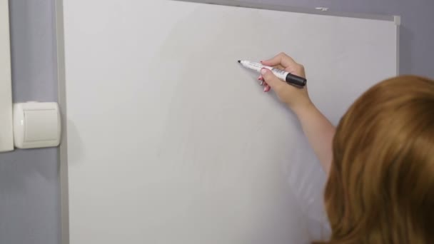 Une femme se tient debout avec son dos et dessine des signes de devise sur un tableau blanc — Video