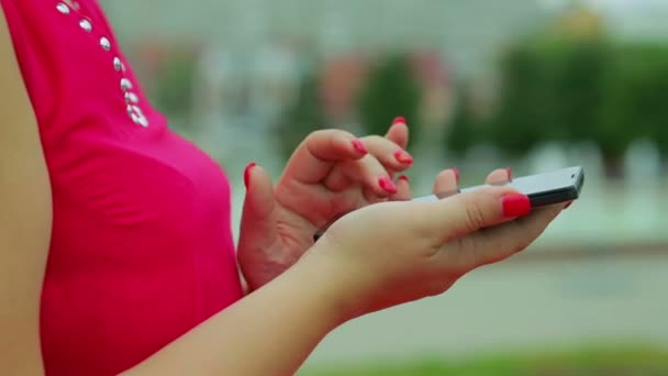 Las manos femeninas con un vestido rojo están en el parque y escriben un mensaje en su teléfono. Primer plano . — Vídeos de Stock