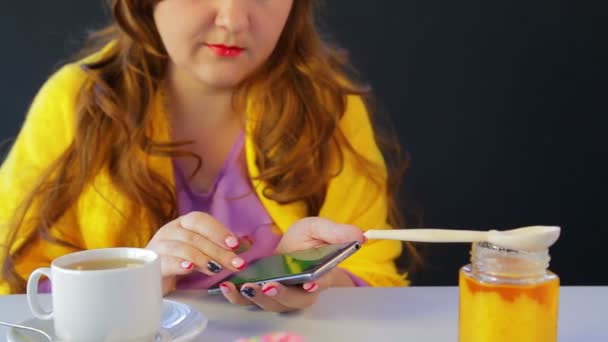 케이크가 있는 식탁에 있는 카페에 있는 소녀가 스마트폰의 뉴스를 통해 흘러나오다. — 비디오