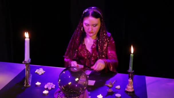 В волшебном салоне цыганка раскладывает карты на черном столе в сиянии — стоковое видео