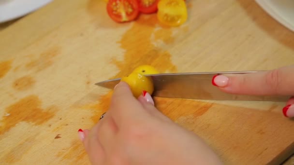 Eine Frau schneidet mit einem Messer eine gelbe und rote Kirschtomate auf einem Holzbrett. — Stockvideo