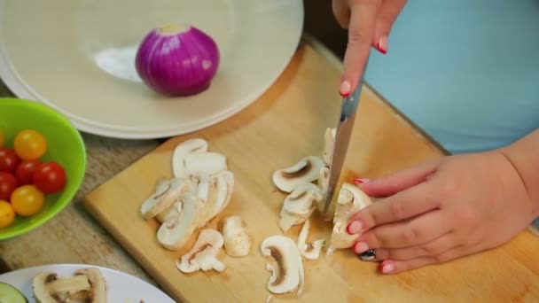 Eine Frau schneidet die Champignon-Pilze mit einem Messer auf einem Holzbrett in Scheiben — Stockvideo