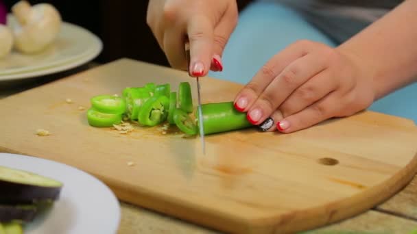 Nő szeletek zöld, hosszú chili paprika késsel egy fa fedélzeten — Stock videók