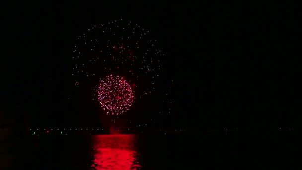 Brillantes fuegos artificiales festivos en el cielo nocturno sobre el río con reflejo en el agua — Vídeo de stock