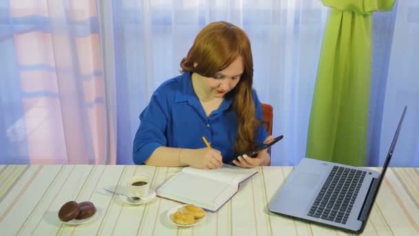 Uma mulher de cabelos castanhos em um café em uma mesa trabalha com um laptop e bebe café . — Vídeo de Stock