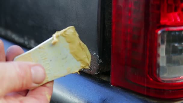 A man puts putty on metal on the rust-free area of the car body — Stock Video