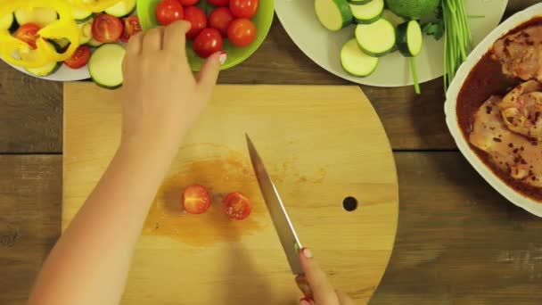 La mano femenina corta un tomate cherry en una tabla de madera por la mitad — Vídeos de Stock