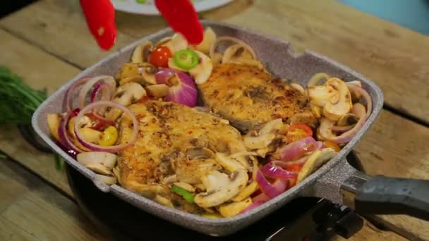 Mão feminina vira bifes de peixe grelhados com pinças e mistura cogumelos com cebola. voltas temporais — Vídeo de Stock