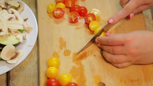 Una mujer está cortando un tomate cereza amarillo y rojo con un cuchillo en una tabla de madera — Vídeos de Stock