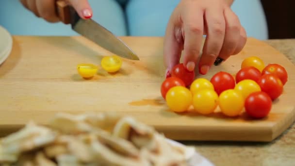 Uma mulher está cortando um tomate cereja amarelo e vermelho com uma faca em uma tábua de madeira. voltas temporais . — Vídeo de Stock