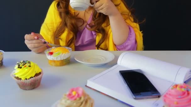 Das Mädchen in einem Café am Tisch trinkt Tee und isst Kuchen mit einem Löffel. — Stockvideo