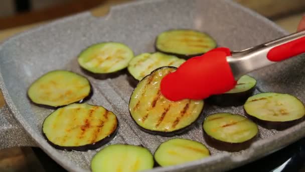 En kvinnlig hand med tång vänder grillning aubergine rostning. tid varv — Stockvideo