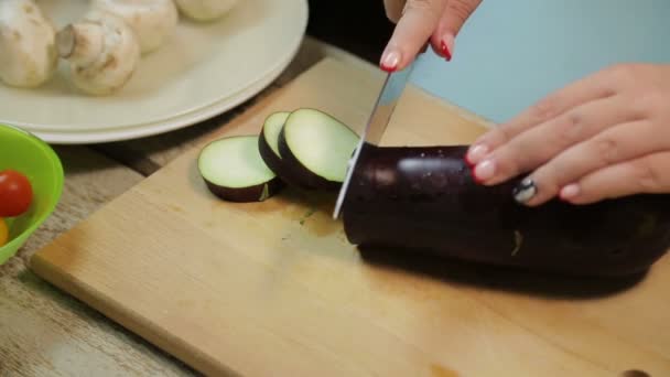 Vrouwelijke hand is het snijden van een donkere aubergine met een mes op een houten plank — Stockvideo