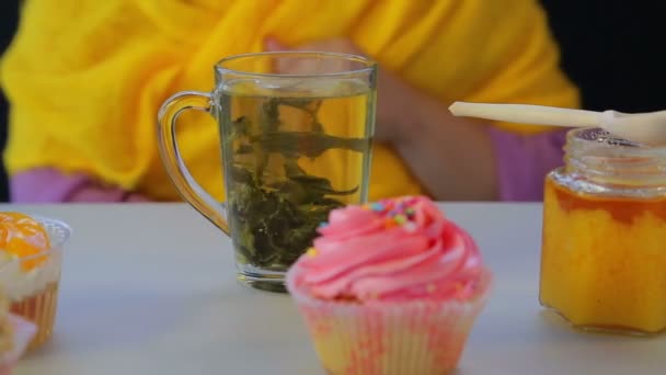 Freshly brewed green tea in a transparent cup on a gray table with cakes. — Stock Video