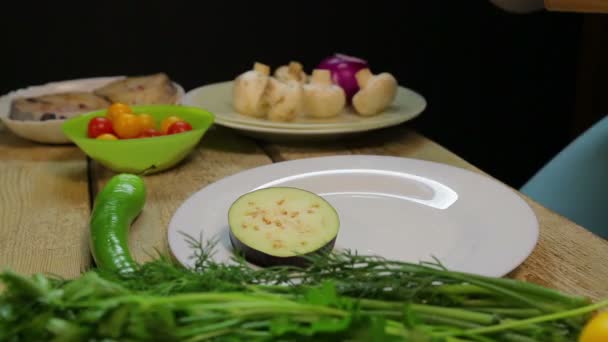 Eine Frau legt Auberginen in Scheiben geschnitten in einen weißen Teller — Stockvideo