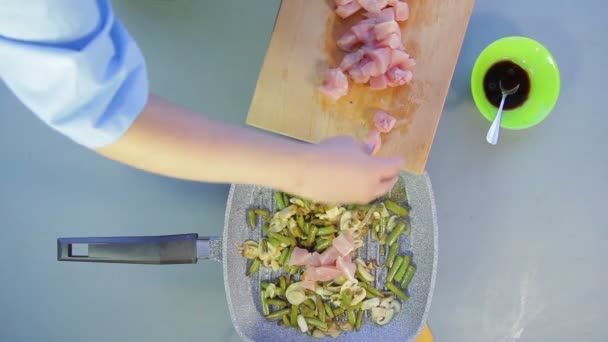 The woman adds pieces of chicken to the pan with green beans and mushrooms — Stock Video