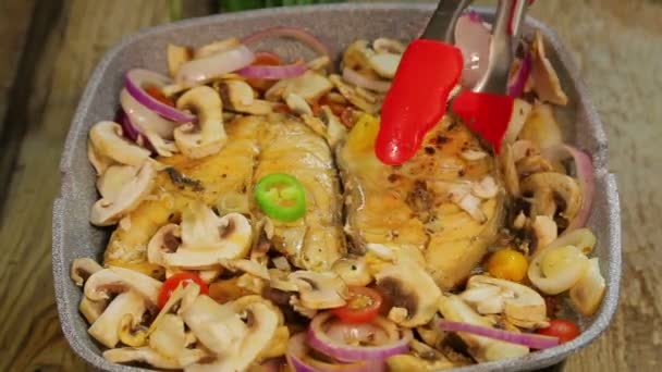 Female hand turns grilled fish steaks with tongs and mixes mushrooms with onions — Stock Video