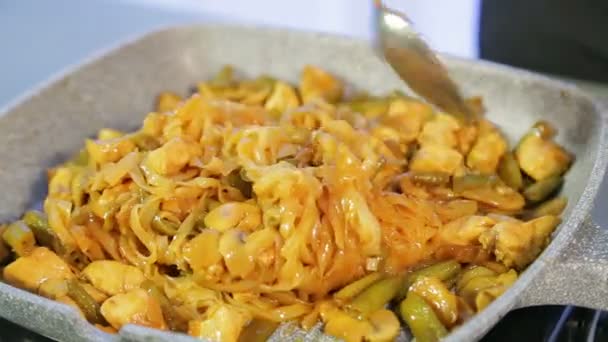 Una mujer está revolviendo fideos de arroz frito con pollo y verduras en una sartén . — Vídeos de Stock