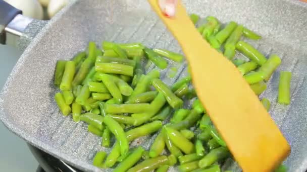 In een pan, groene string bonen worden gemalen in olie en geroerd met een houten spatel — Stockvideo
