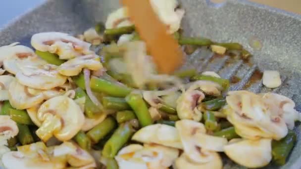 Жінка змішує зелені боби з грибами на сковороді . — стокове відео