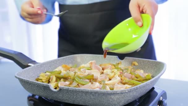 Uma mulher mistura uma espátula de madeira em uma frigideira com filé de frango com feijão e cogumelos e o derrama com molho de soja. . — Vídeo de Stock