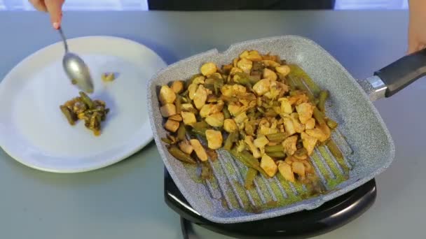 Een vrouw verschuift gebakken kip met groene bonen en champignons uit een koekenpan in een witte plaat — Stockvideo