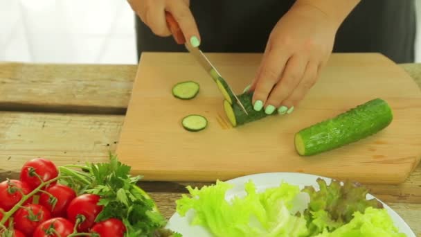 Primer plano de las manos femeninas cortan pepinos con un cuchillo para hacer ensalada. Cámara se mueve a dolly — Vídeo de stock