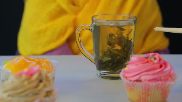 Thé vert fraîchement infusé dans une tasse transparente sur une table grise avec des gâteaux — Video