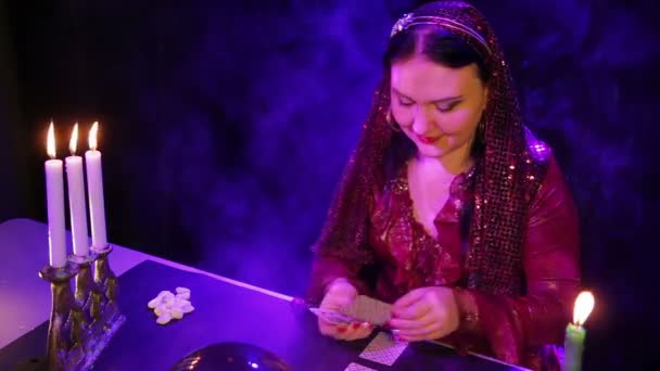 Ένας γύφτος σε ένα κόκκινο φόρεμα σε ένα μαγικό κομμωτήριο των κεριών διαβάζει το μέλλον σχετικά με τις κάρτες — Αρχείο Βίντεο