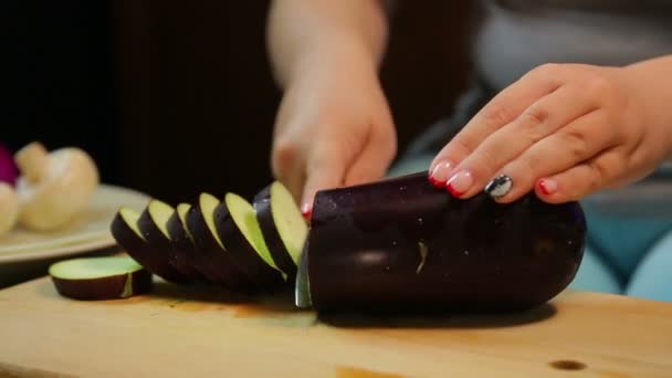 Female hand is cutting a dark eggplant with a knife on a wooden board. — Stock Video