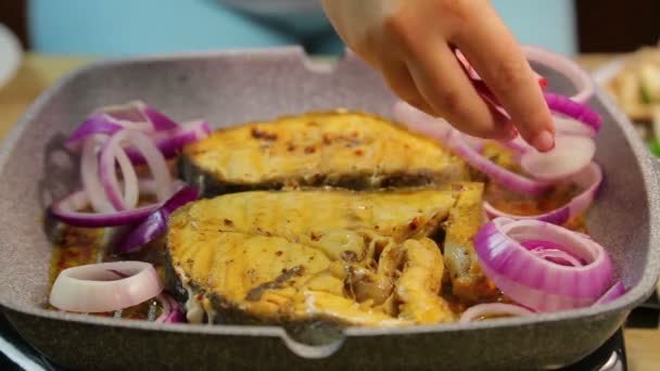 Женская рука кладет в рыбу нарезанный лук и черри томатные кольца — стоковое видео