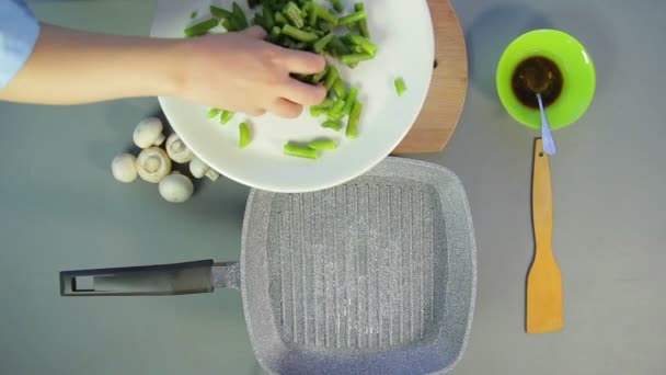 Eine Frau legt frische grüne Bohnen in eine Pfanne mit kochendem Öl — Stockvideo