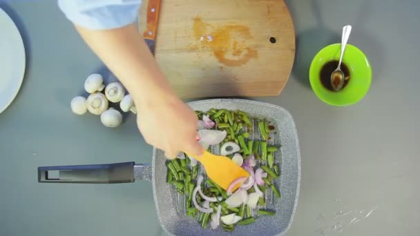 Женская рука шевелит жарким луком и зеленой фасолью с деревянной лопаткой — стоковое видео