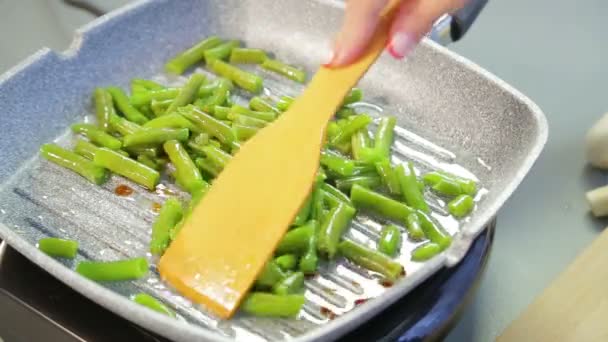 In a pan, green string beans are ground in oil and stirred with a wooden spatula — Stock Video