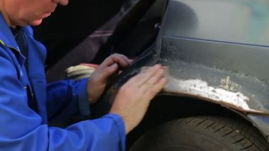 Bir adam zımpara kağıdı ile araba gövdesinde pas izlerini temizler