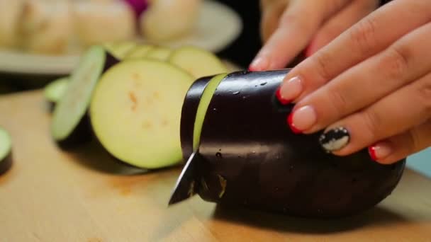 A woman is slicing a medium eggplant with a knife on a wooden board. — Stock Video