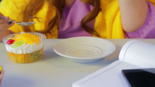 The girl in a cafe at the table drinks tea and eats cakes with a spoon. — Stock Video