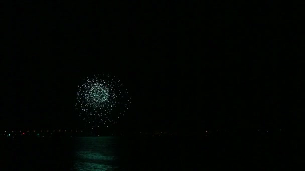 Un fuego que dispersa fuegos artificiales festivos en el cielo nocturno sobre el río se refleja en el agua. Vueltas de tiempo — Vídeos de Stock