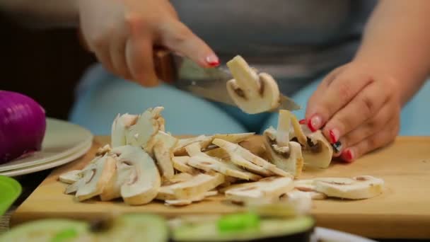 Uma mulher corta os cogumelos champignon em fatias com uma faca em uma placa de madeira . — Vídeo de Stock