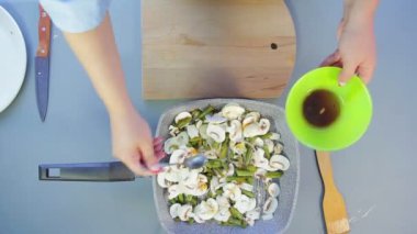 Bir kadın ahşap bir spatula ile bir tavada mantar ve soğan karıştırır ve soya sosu ekler