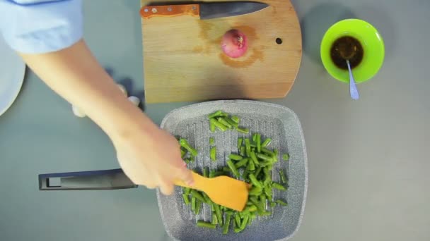 Mulher mexendo feijão verde assando em uma frigideira com uma espátula de madeira . — Vídeo de Stock