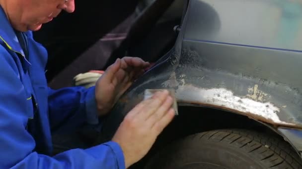 Ένας άνθρωπος καθαρίζει ίχνη σκουριάς από το σώμα του αυτοκινήτου με χαρτί Έμερι. — Αρχείο Βίντεο