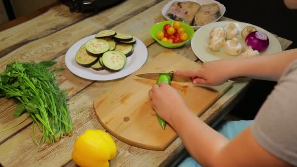 En kvinna skär grön chili paprika med en kniv på en trä kartong. — Stockvideo