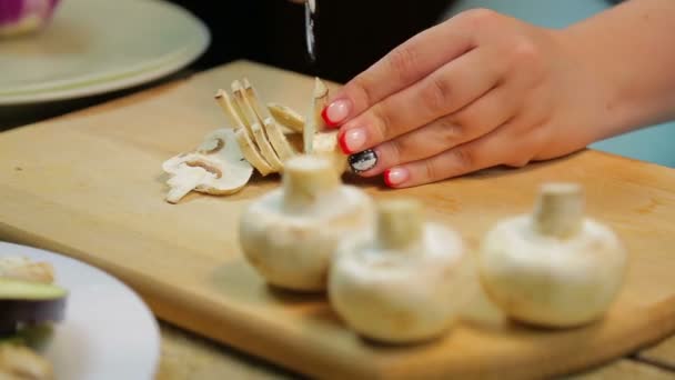 Женщина режет шампиньонские грибы на кусочки ножом на деревянной доске — стоковое видео