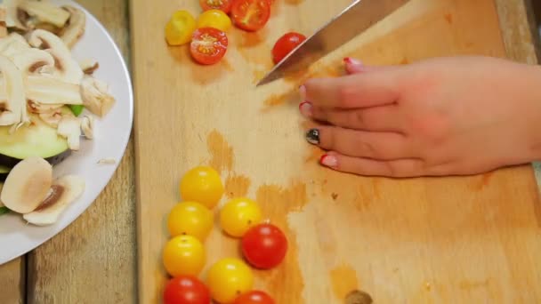 Женщина режет жёлтый и красный помидор черри с ножом на деревянной доске — стоковое видео
