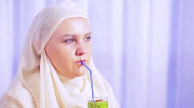 Hafif bir eşarp bir genç Müslüman kadın bir meyve smoothie içecekler ve gülümsüyor