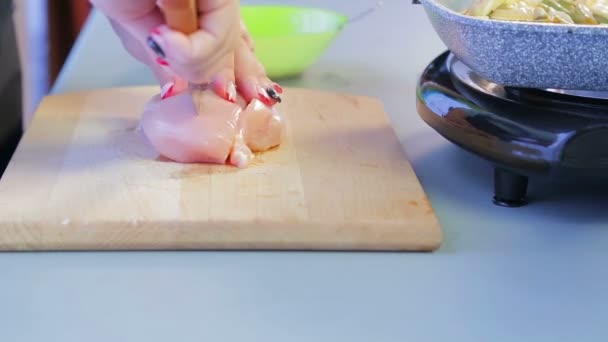 Vrouw plakjes kipfilet met een mes op een houten plank — Stockvideo